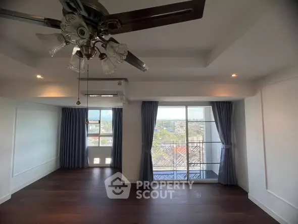 Spacious living room with ceiling fan and large windows offering city views.