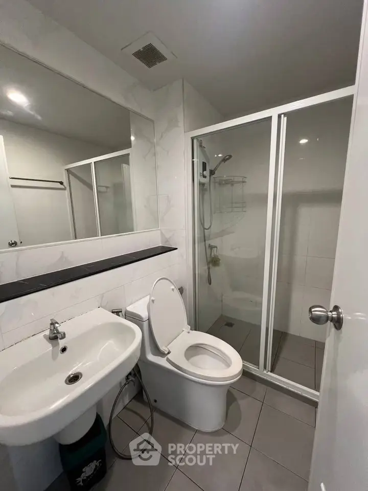 Modern bathroom with sleek fixtures and glass shower enclosure in contemporary apartment.
