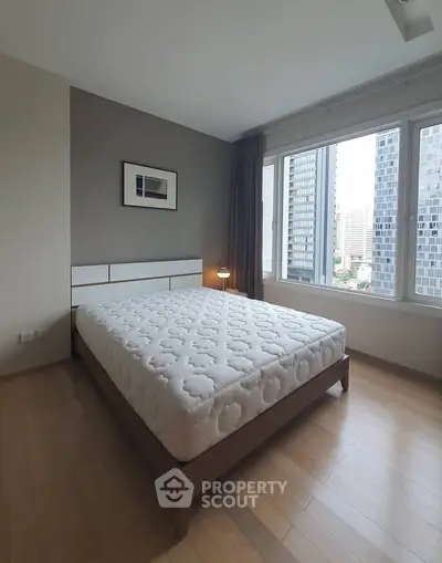 Spacious bedroom with large windows offering city views, featuring a comfortable bed and modern decor.
