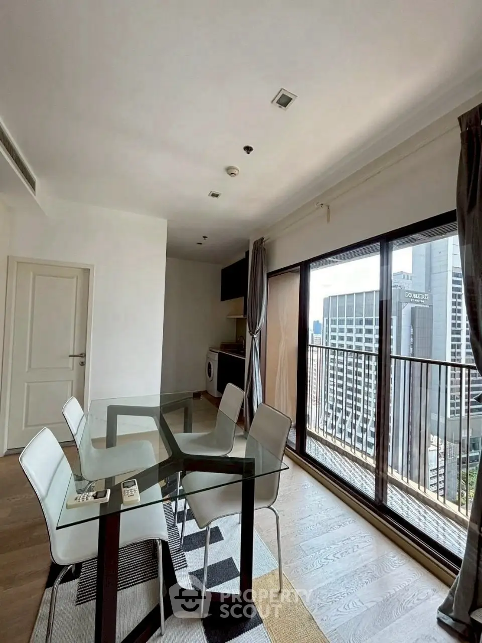 Modern dining area with glass table and city view balcony in high-rise apartment.