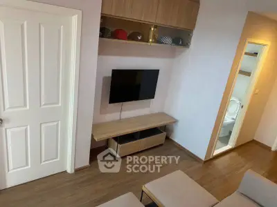Modern living room with wall-mounted TV and wooden flooring, adjacent to a bathroom.