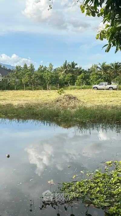 Scenic view of a serene rural landscape with a pond and a pickup truck under a clear blue sky.