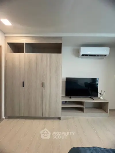 Modern bedroom with sleek wardrobe and mounted TV, featuring minimalist design and air conditioning.