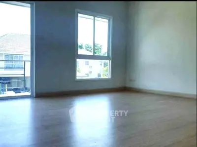 Spacious empty room with large window and wooden flooring, offering natural light and potential for customization.