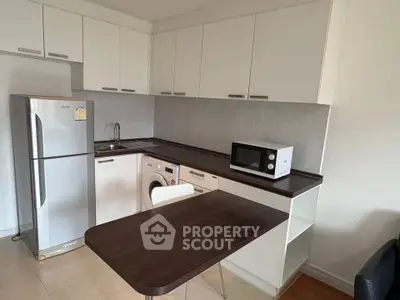 Modern kitchen with sleek cabinets, fridge, washing machine, and microwave in compact layout.