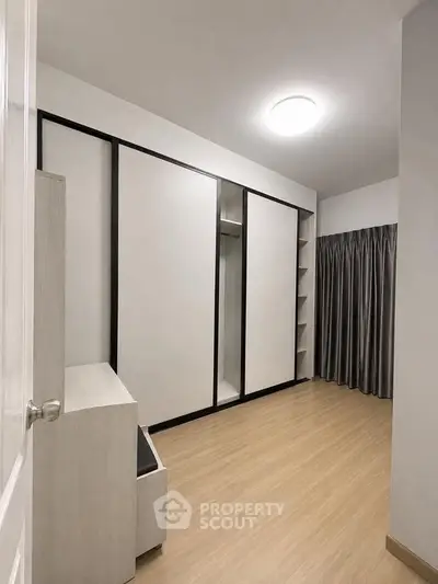 Spacious modern bedroom with sleek built-in wardrobe and elegant wooden flooring.
