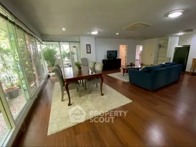 Spacious living room with elegant dining area and large windows overlooking greenery.