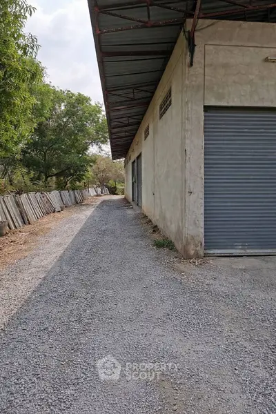 Industrial warehouse exterior with gravel driveway and metal roll-up doors.