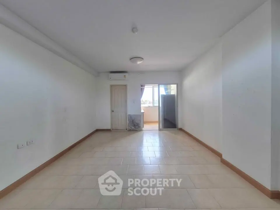 Spacious empty living room with tiled flooring and balcony access, perfect for customization.