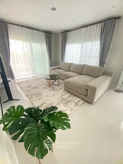 Elegant living room with large sectional sofa and modern decor, featuring floor-to-ceiling windows and lush greenery.