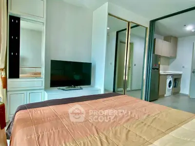 Modern bedroom with TV and mirrored closet, open view to kitchen with washing machine.