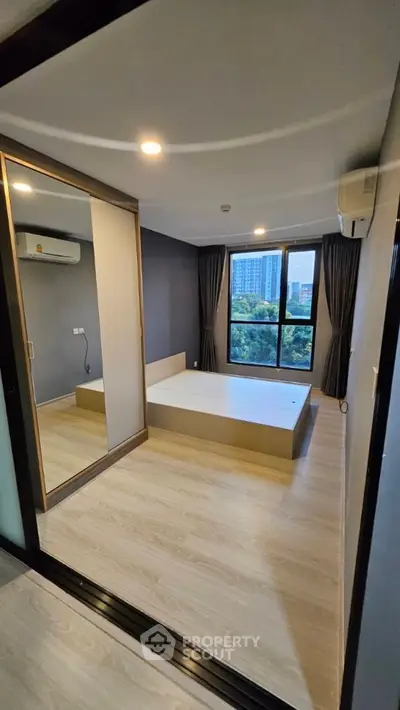 Modern bedroom with large window and mirrored closet in urban apartment