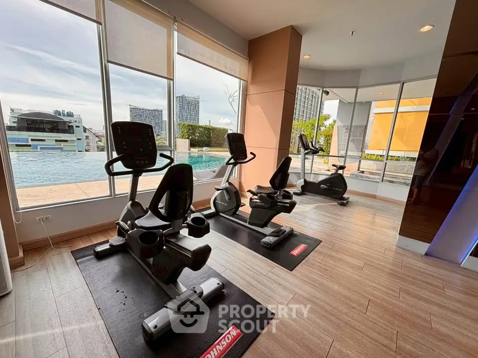 Modern gym with exercise bikes overlooking a stunning pool view in a luxury apartment complex.