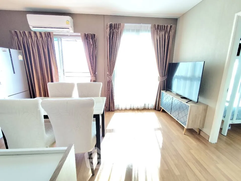 Bright modern living room with dining area and large TV, featuring elegant curtains and wooden flooring.
