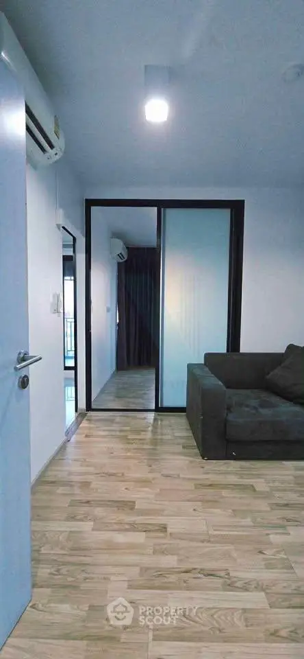 Modern living room with wooden flooring and sleek glass partition in a contemporary apartment.