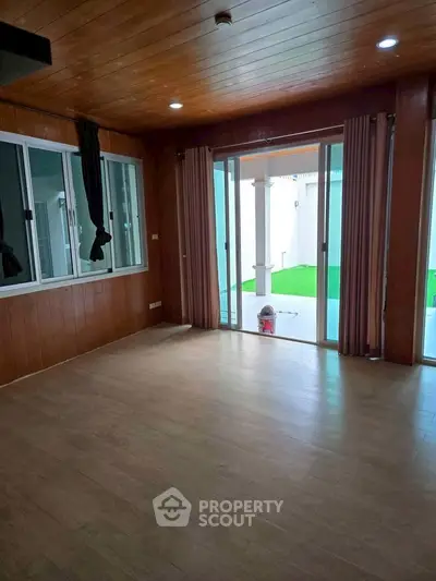 Spacious living room with wooden ceiling and large sliding glass doors opening to a green outdoor area.