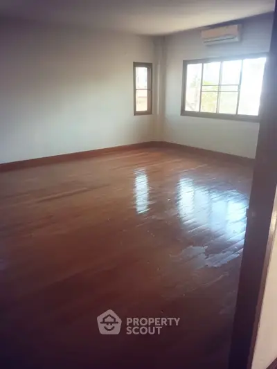 Spacious empty room with polished wooden floors and large windows, perfect for customization.