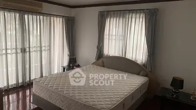 Spacious bedroom with large windows and elegant curtains, featuring a comfortable bed and stylish bedside tables.