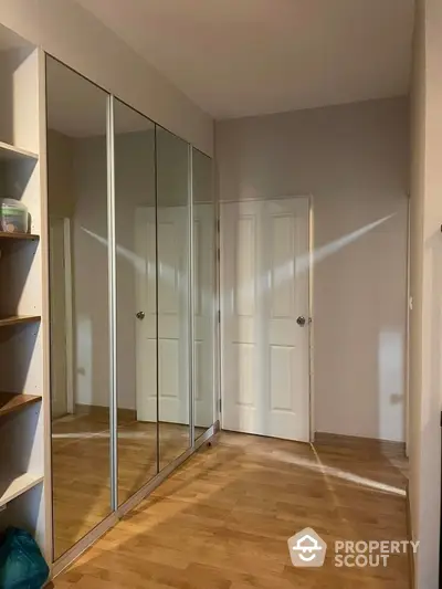 Spacious bedroom with mirrored closet doors reflecting natural light, enhancing the warm wooden flooring and neutral walls.