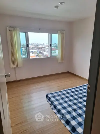 Spacious bedroom with wooden flooring and large window offering city views.