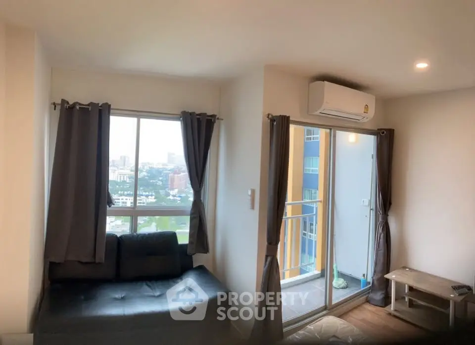 Modern living room with balcony and city view, featuring sleek furniture and air conditioning.