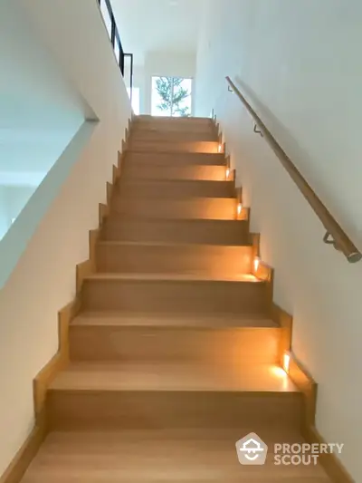 Elegant wooden staircase with ambient lighting enhancing the warm tones, leading to a bright, inviting upper level in a modern home.