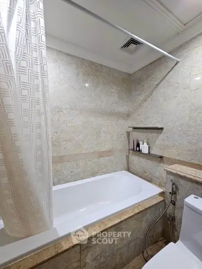 Elegant bathroom with marble tiles and bathtub, featuring a modern shower curtain and built-in shelf.