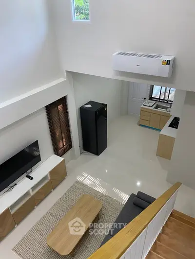 Modern living room with open kitchen, featuring sleek furniture and appliances.