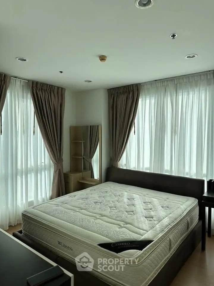 Spacious bedroom with large windows and elegant curtains, featuring a comfortable bed and modern decor.