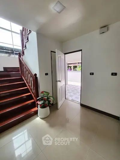 Bright hallway with wooden staircase and potted plant, leading to outdoor area.