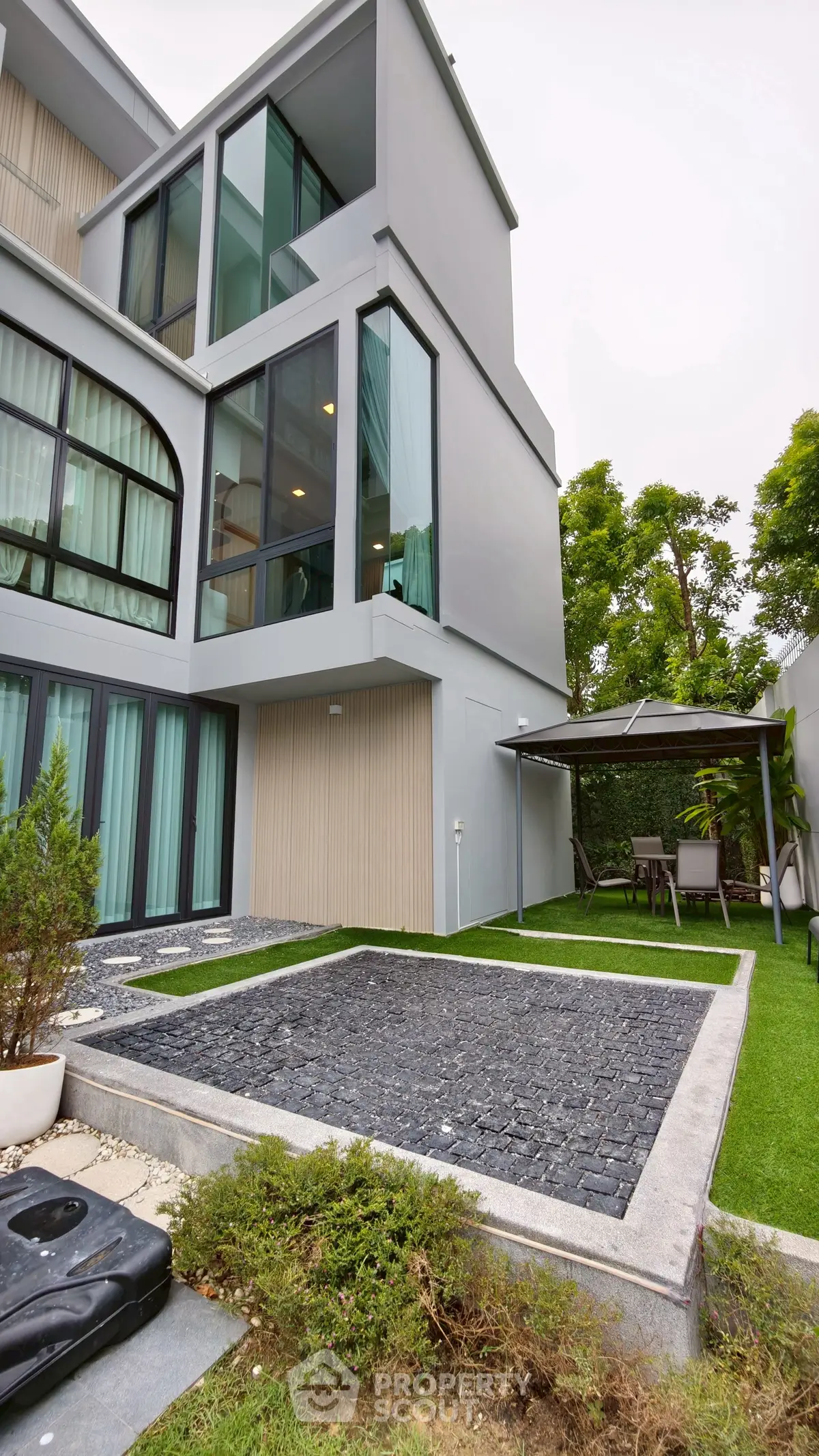 Modern multi-story building with garden and patio area, featuring large windows and sleek design.