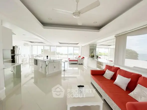 Spacious modern living room with panoramic windows and red sofas, offering a stunning ocean view.