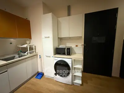 Modern kitchen with sleek cabinets, washing machine, and microwave, featuring efficient use of space.