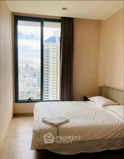Cozy bedroom with large window offering stunning city view in modern high-rise apartment.