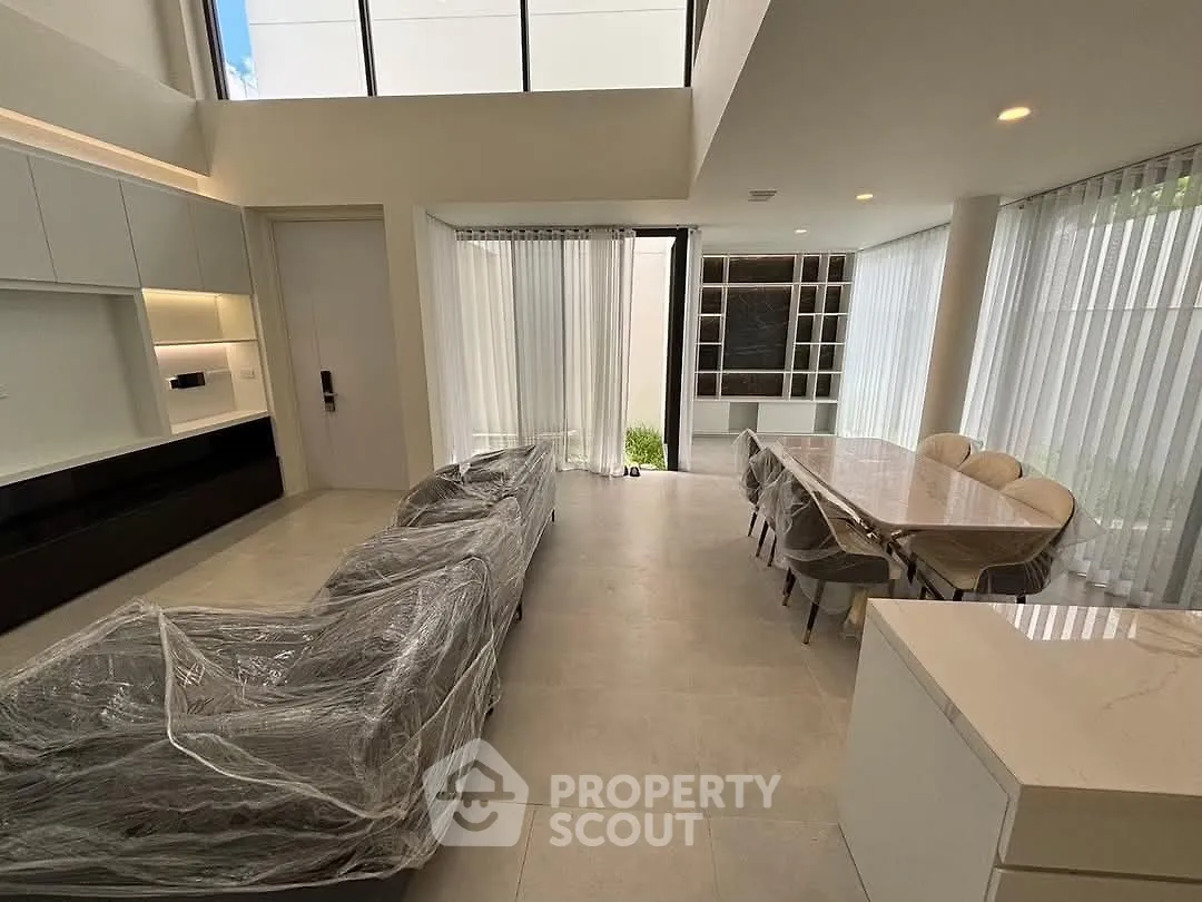 Luxurious modern living room with high ceilings and elegant dining area, featuring floor-to-ceiling windows.