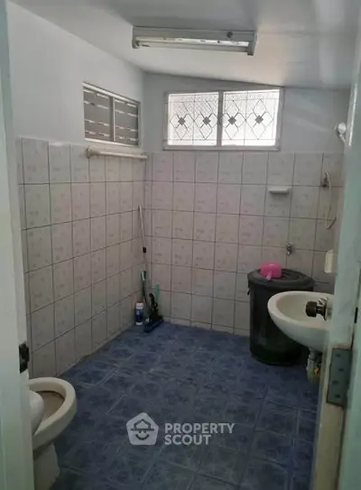 Spacious bathroom with tiled walls and floor, featuring a toilet and sink.