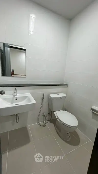 Modern bathroom with white tiles, sleek sink, and toilet in a contemporary apartment.