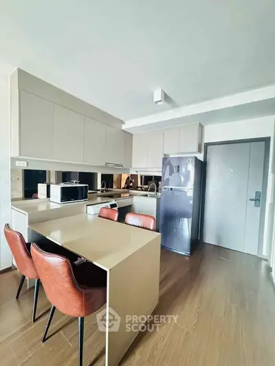 Modern kitchen with sleek cabinetry, dining area, and stainless steel appliances in a stylish apartment.