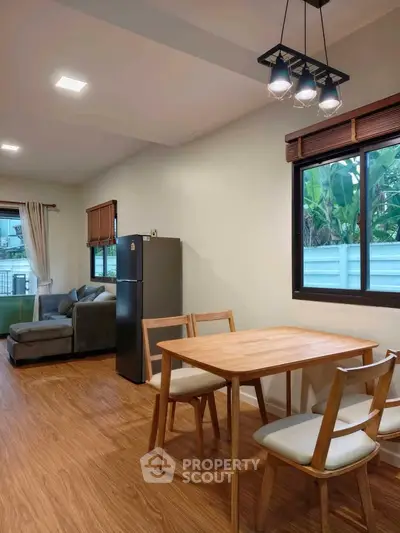 Modern living room with dining area and large window, featuring wooden flooring and contemporary furniture.