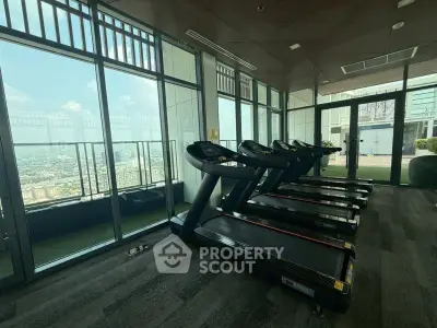 Modern gym with treadmills and panoramic city view from large windows.