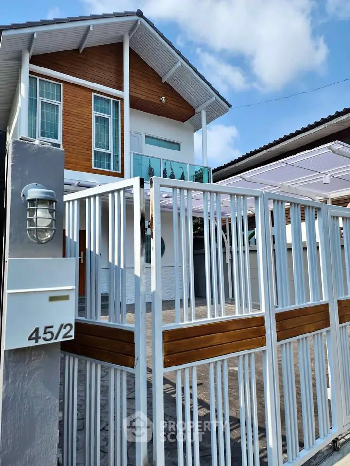 Modern two-story house with stylish gate and wooden accents under a clear blue sky.