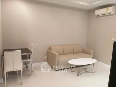 Modern living room with beige sofa and dining set, featuring minimalist design and air conditioning.