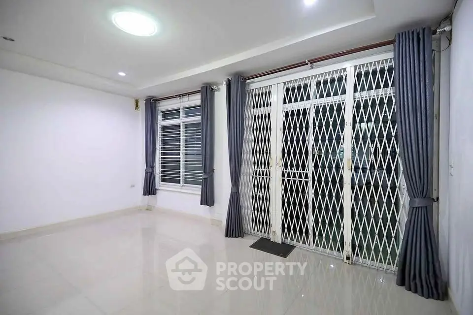 Spacious modern living room with large windows and sliding doors, featuring sleek tile flooring and elegant curtains.