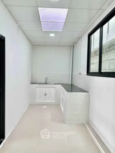Modern minimalist kitchen with sleek white cabinetry and large window.