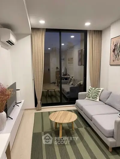 Modern living room with stylish decor, featuring a cozy sofa, sleek TV setup, and large glass doors leading to a balcony.