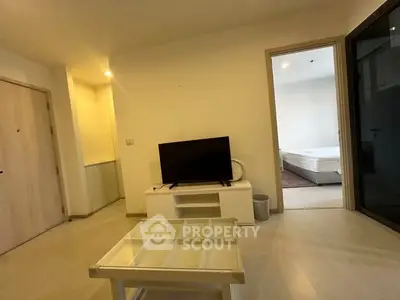 Modern living room with TV and glass coffee table, leading to a bedroom.