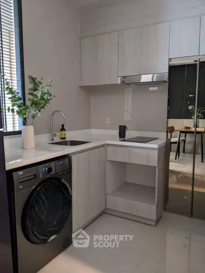 Modern kitchen with sleek cabinetry and built-in appliances, featuring a washing machine and elegant decor.