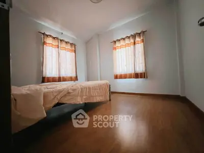 Spacious bedroom with wooden flooring and natural light from two windows.