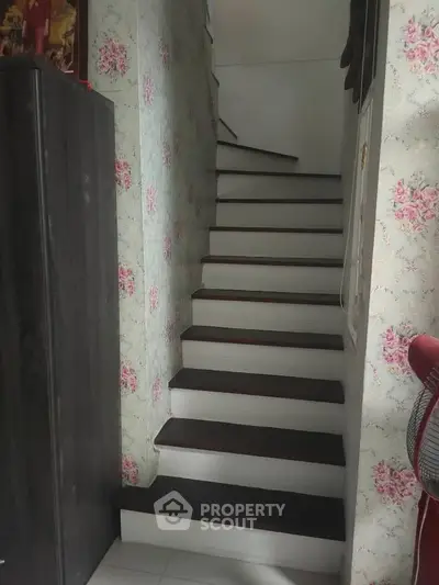 Charming staircase with floral wallpaper and dark wood accents in cozy home interior.