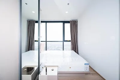 Bright and modern bedroom with large window offering stunning city views, featuring a comfortable bed and sleek design.